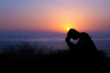 Man Praying by the Sea at Sunset clipart