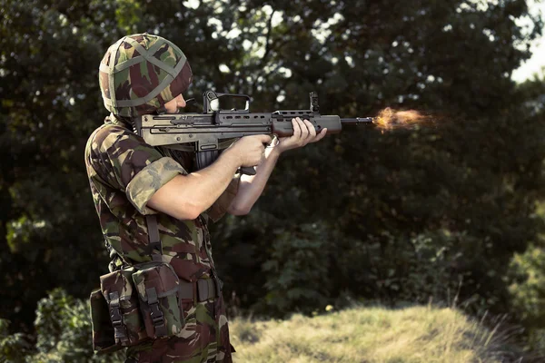Mladý voják stojící se zbraní a střelba — Stock fotografie