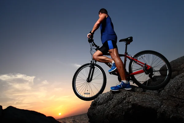 자전거와 함께 바위에 서 있는 젊은 선수 — 스톡 사진