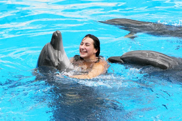 Feliz hermosa joven se ríe y nada con delfines en blu — Foto de Stock