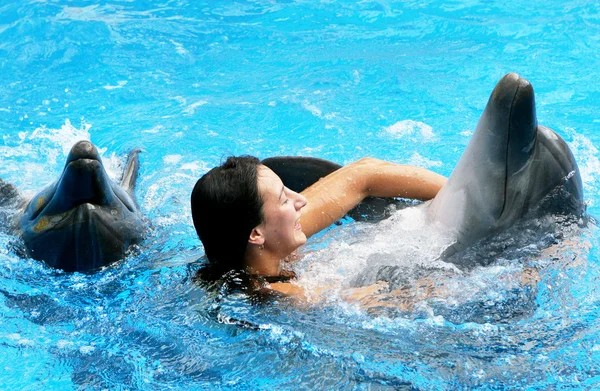 Happy beautiful young girl laughs and swims with dolphins in blu — Stock Photo, Image