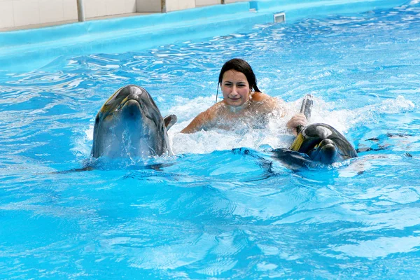 Happy beautiful young girl laughs and swims with dolphins in blu — Stock Photo, Image