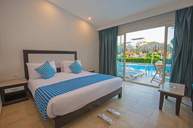 Teras ve havuz manzaralı lüks bir otel odasında çift kişilik yatak.