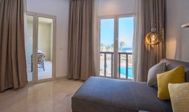 Lüks apartmandaki oturma odası salonu balkon terası ve deniz manzarasıyla döşenmiş iç tasarım dekorasyonunu gösteriyor.