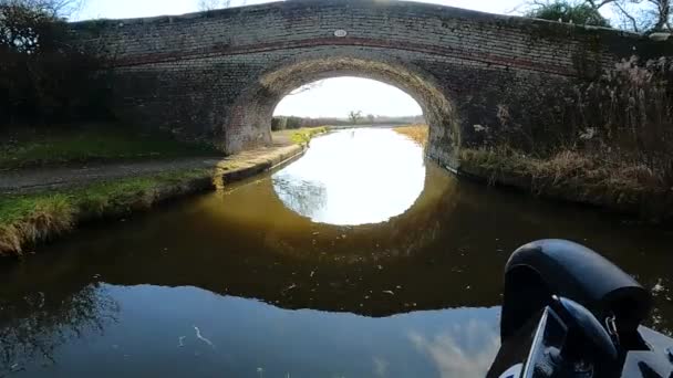 古い石の道路橋と英国の水路の運河に英語の田舎の風景を示す狭い船の弓からの眺め — ストック動画