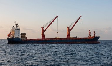 Yelken vinçleri ve üst yapısıyla denizde demirli büyük bir kargo konteynırı gemisi.