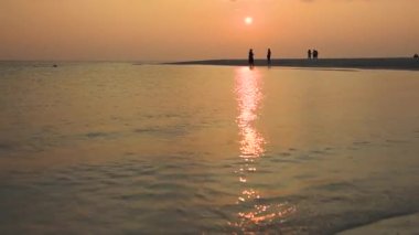 Güneş batarken tropikal okyanus üzerindeki tropikal kumlu güzel kumlu plajın panoramik görüntüsü yansımalı.