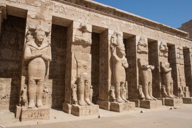 Antik Mısır Medinatı Habu Tapınağı 'nda avlu bölgesinde kolonları olan Ramses II' nin büyük heykelleri.