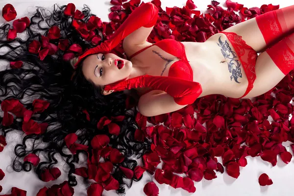 Girl with tattoos in red lingerie in the petals of red roses — Stock Photo, Image