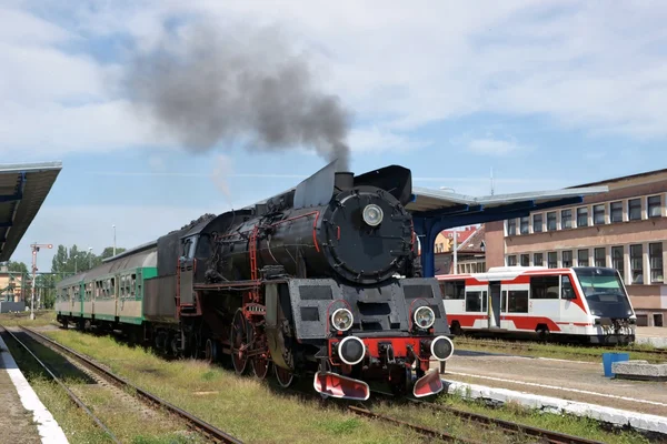 Σιδηροδρόμων, ατμού ατμομηχανή με βαγόνια που στέκεται ο σταθμός, το ηλεκτρικό τρένο στο παρασκήνιο — Φωτογραφία Αρχείου