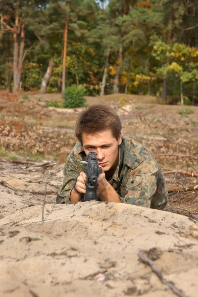 Teini-ikäinen, poika makaa taisteluasussaan ja kivääri, Air Soft Gun — kuvapankkivalokuva