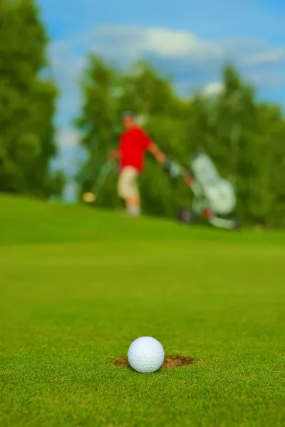 Golf, ball lying on the green next to hole, in the background goes golfer — Stock Photo, Image