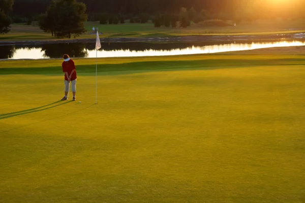 Golf, vrouw golfspeler stak de bal in het gat bij zonsondergang als achtergrond — Stockfoto