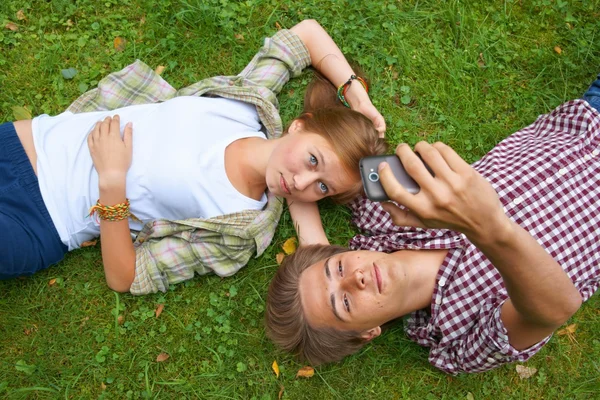 Chlapec a dívka, teens, ležící na trávě a zkontrolujte volání — Stock fotografie