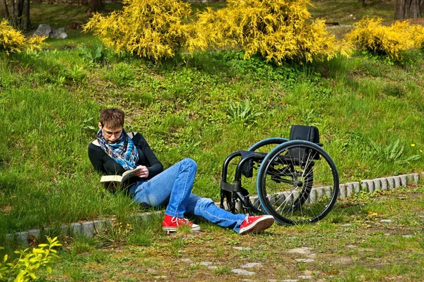 Femme handicapée lisant un livre dans le parc, en fauteuil roulant — Photo