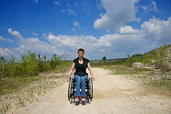 Mujer discapacitada y sonriente montando una silla de ruedas, camino en una cantera — Foto de Stock