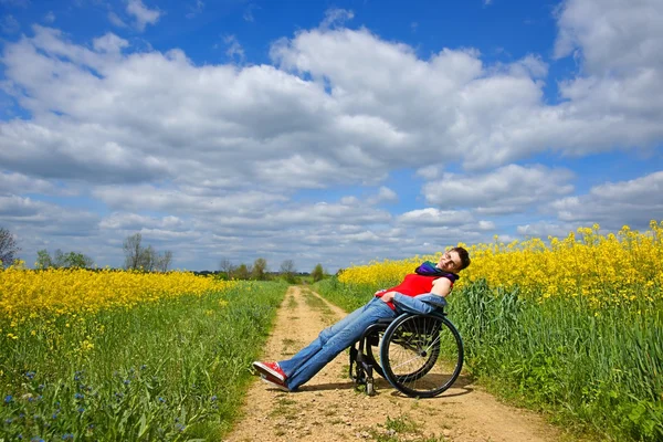 Disabled woman sunbathing on a wheelchair, rape field, spring — Stock Photo, Image