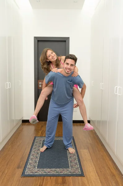 Jovem casal feliz com ela no piggyback em pijamas — Fotografia de Stock