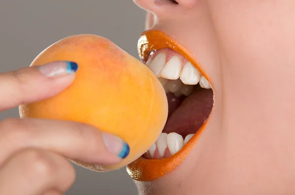 Beautiful young woman eating a peach. — Stock Photo, Image