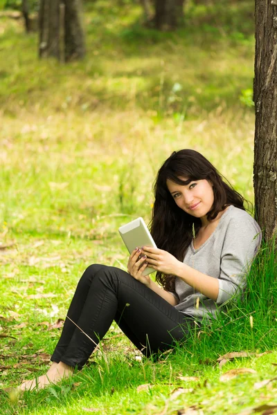 Счастливая молодая женщина с цифровым планшетом сидит на траве в парке — стоковое фото