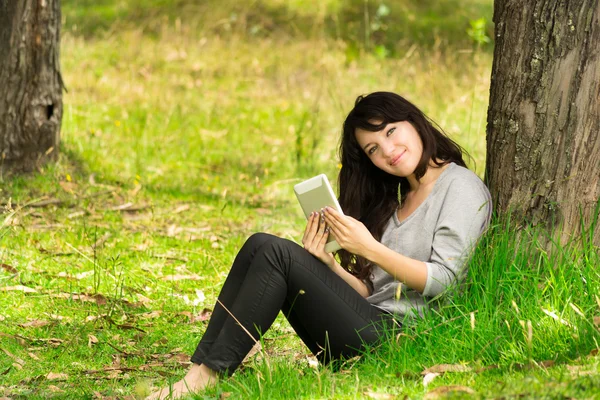 Mujer joven feliz con tableta digital sentado en la hierba en el parque —  Fotos de Stock