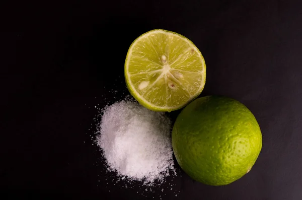 Citrus kalk fruit helft op zwarte achtergrond, kleine groene citroenen met zout — Stockfoto