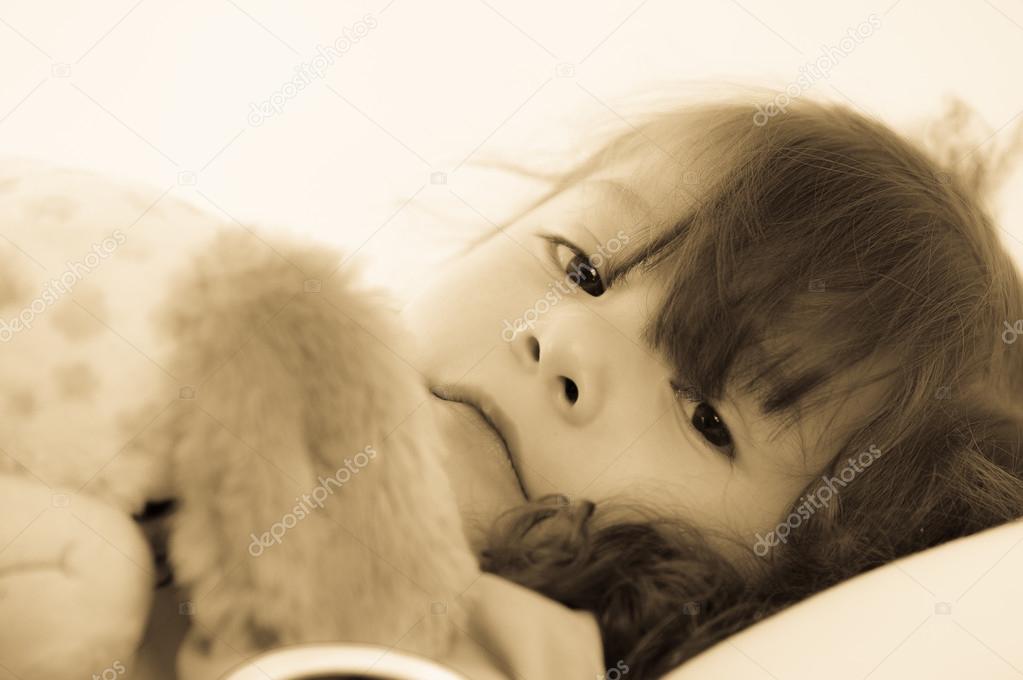 Sad little girl lying in bed in the bedclothes. colortoned