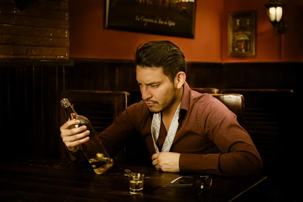 Latino cara beber tiros olhando para garrafa — Fotografia de Stock