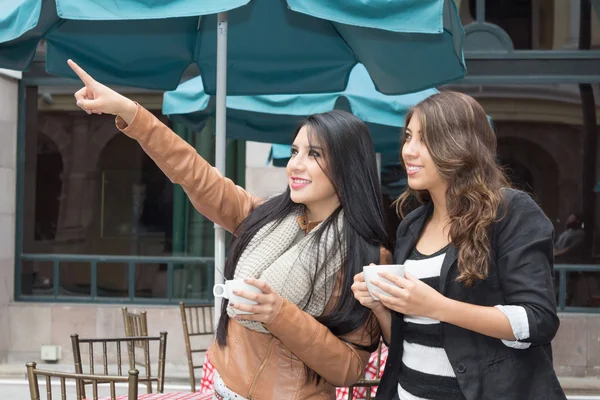 Duas meninas segurando xícaras de café apontando um lugar — Fotografia de Stock