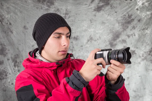 Close-up de jovem bonito homem vestindo casaco vermelho e gorro preto sobre fundo cinza — Fotografia de Stock