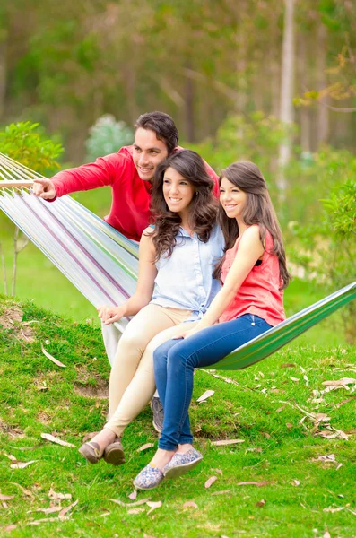 Dos hermosas chicas y un hombre joven en hamaca al aire libre — Foto de Stock