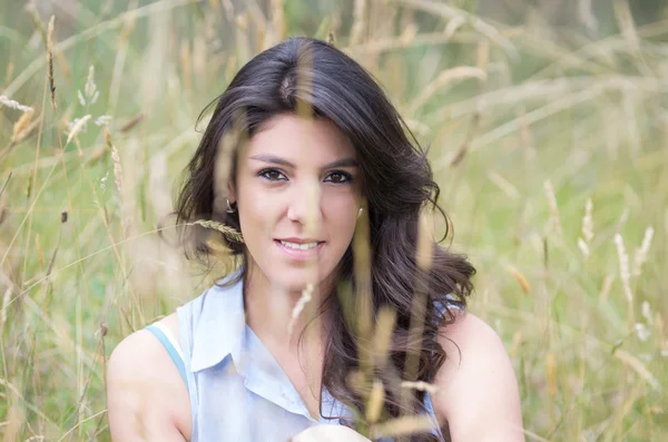 Mooie jonge meisje zit in een veld — Stockfoto