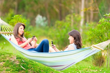 Two young girls resting on a hammock smiling clipart