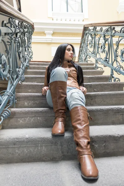 Молода дівчина в коричневих шкіряних чоботях і куртці сидить на сходах — стокове фото