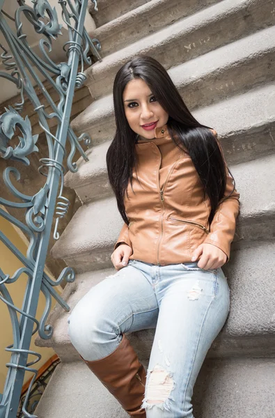 Молодая девушка в коричневых кожаных сапогах и куртке сидит на лестнице — стоковое фото