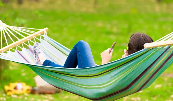 Junges Mädchen liegt mit Handy in der Hängematte — Stockfoto