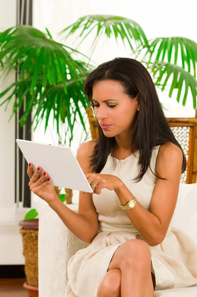 Vacker ung elegant kvinna håller en digital tablet som sitter på soffan — Stockfoto