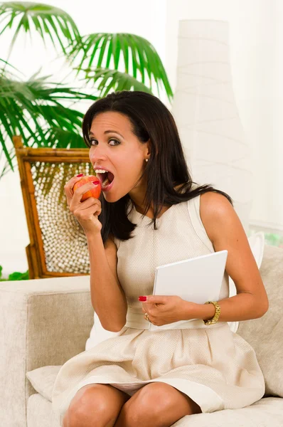 Bella giovane donna elegante seduta in soggiorno con tablet digitale e mangiare una mela — Foto Stock