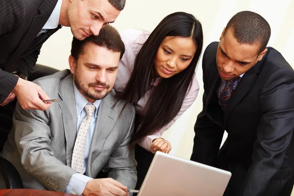 Reifer Geschäftsmann zeigt seinem multiethnischen Business-Team etwas auf dem Laptop — Stockfoto