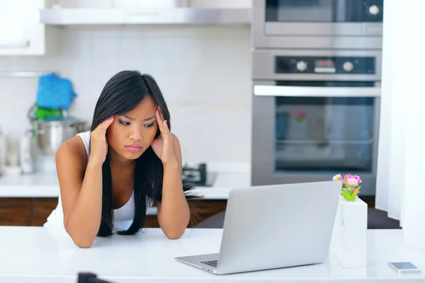 Hermosa joven asiática mujer teniendo un dolor de cabeza en casa delante de su ordenador — Foto de Stock