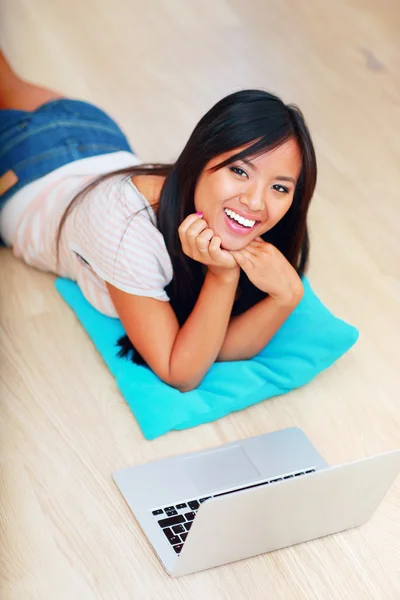 Азиатка лежит на полу с ноутбуком — стоковое фото