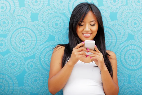 Asian woman with smartphone standing against blue background — Stock Photo, Image