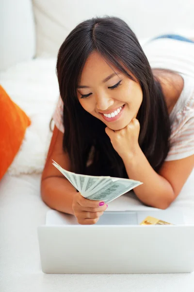 Asian woman holding stack of dollars while using her laptop — Stock Photo, Image