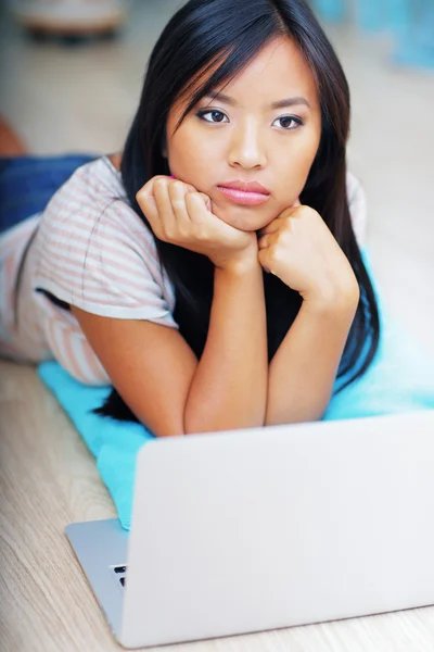 Dreamy young asian woman lying on the floor with laptop — Stock Photo, Image
