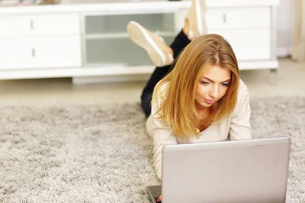 Donna con computer portatile sdraiato su tappeto — Foto Stock