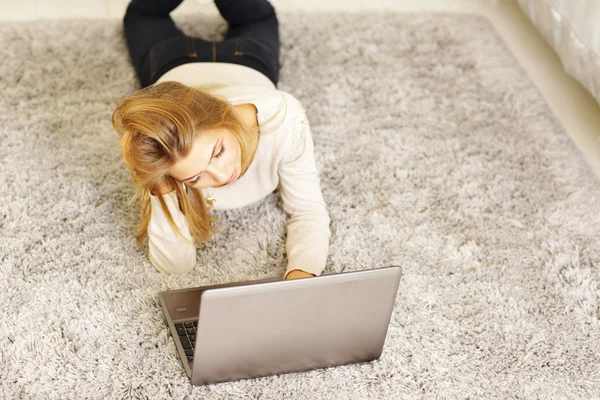 Donna con computer portatile sdraiato su tappeto — Foto Stock