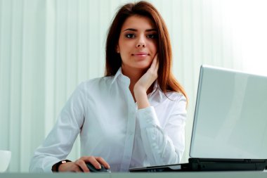 İş kadını elinde dizüstü bilgisayarla masada oturuyor.