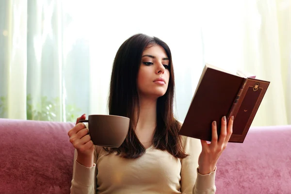 Woman holding cup of coffee and reading book — Stock Photo, Image