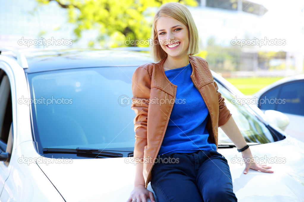 Young happy girl sitting on the hood of a car.