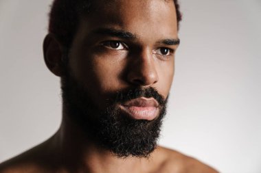 Siyah tişörtsüz sakallı adam beyaz arka planda yalnız poz veriyor ve yan tarafa bakıyor.